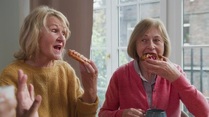 Three elderly retired women sitting at table chatting joyfully. Multiracial senior women chill together talking. Female aged friends having tea time at home and communicating smiling
