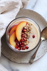 Smooth yogurt topped with peach slices, pomegranate seeds, and granola on a ceramic plate