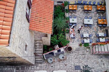 Aerial view of a quaint outdoor cafe with stone walls and tiled roofs, featuring tables and chairs...