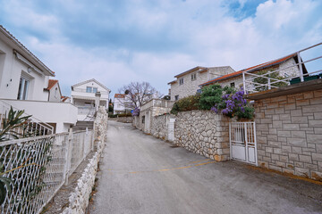 A narrow street in a Mediterranean village with stone houses and blooming purple flowers.