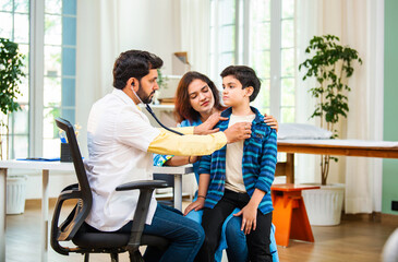 Male doctor checking boy’s symptoms with stethoscope as mother watches in hospital clinic setting
