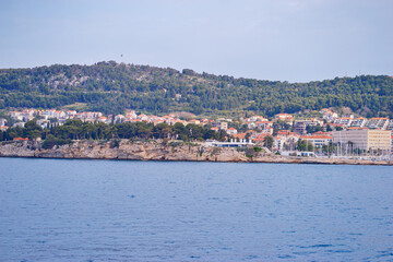 Coastal cityscape with buildings and lush green hills by the sea.