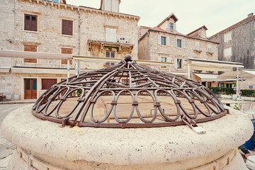 A historic stone well with an ornate metal cover in a European courtyard, surrounded by old stone...