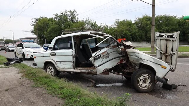 The aftermath of a traffic accident on a city road, close-up. A car with a broken front end and an open hood is at the scene of the accident. Broken windshield.