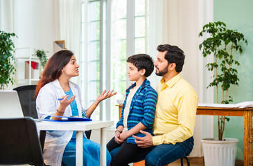 Caring Indian female doctor discussing diagnosis and medication with child patient and his father