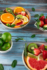 Bowls with slices of citrus fruits, strawberries and limes on blue rustic background. Fresh and summery composition with vibrant fruits. Concept of healthy eating and freshness