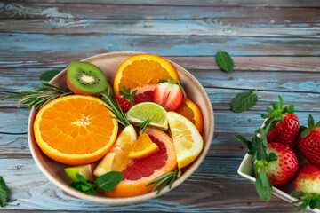 Citrus fruits and strawberries in ceramic bowls, with aromatic herbs on blue wooden background. Copy space. Concept of nutrition, vitamins and balanced diet