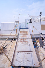 A docked white boat with a ramp leading to the shore, set against a coastal backdrop.