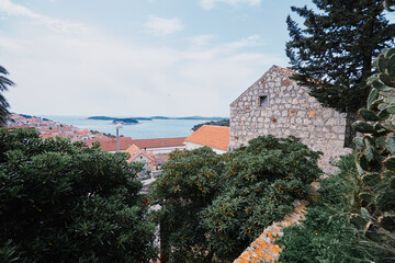 Obraz premium Scenic view of a coastal town with stone houses and lush greenery, overlooking the sea and distant islands under a clear sky.