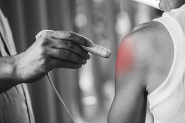A physical therapist performs laser therapy on a patients shoulder to reduce pain, decrease...