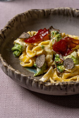 Close up of creamy pasta with truffles, crispy bacon, and broccoli