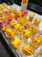 Colorful fruit cups filled with fresh mango, pineapple, and watermelon showcase tropical flavors in...