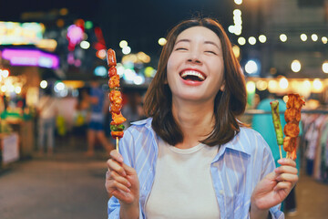 Happy young Asian woman walking in the night market,woman enjoying street food at local night market