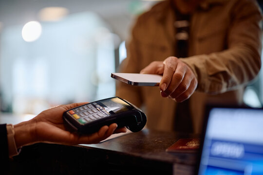 Close up of hotel guest paying contactless with mobile phone at reception desk.