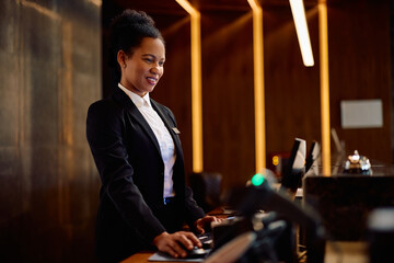 Black female concierge using computer while working at hotel reception.