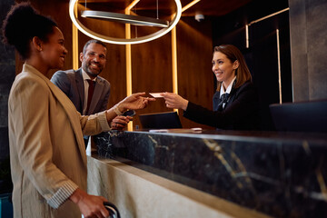 Happy black businesswoman receiving room cardkey while checking in at hotel.