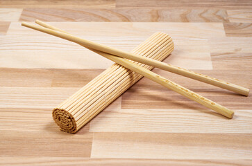 Rolled bamboo sushi mat (makisu) is placed on a light wooden surface with a pair of wooden chopsticks