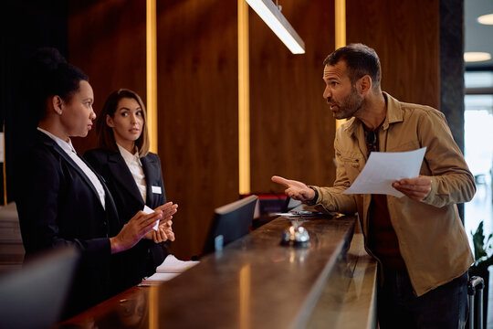 Dissatisfied hotel guest having arguing with receptionists at front desk.