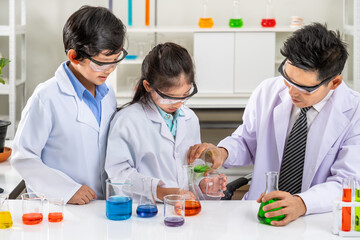 Young scientists in laboratory – Asian kids and teacher conducting chemistry experiment with...