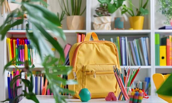 a yellow backpack surrounded by various school supplies, Copy space text, including pencils, an apple, and books, set against a green chalkboard background