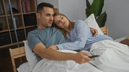 Fototapeta premium Couple relaxing in a cozy bedroom watching tv as the woman rests her head on the man's shoulder enjoying a peaceful moment together indoors.