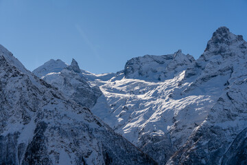 Snow-capped peaks with majestic blue slopes rise above jagged slopes of North Caucasus Range. Mountain tops are covered with eternal glaciers. Dombay. Karachay-Cherkessia.
