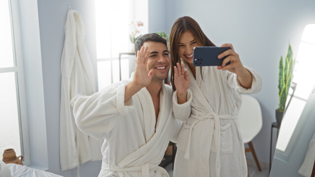 Man and woman smiling in spa taking a selfie in robes, capturing joyful moment in a wellness center's relaxing interior with bright lighting and modern decor.