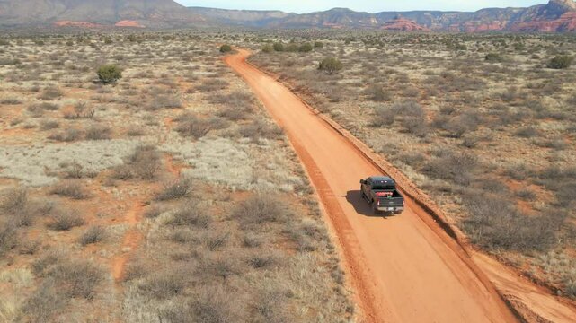 A 60fps drone shot following black Ford F250 driving on a red dirt road in the desert near Sedona with striking mountains in the background