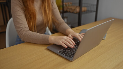 Woman using laptop in a modern office setting, focusing on work with hands typing on keyboard at desk, capturing an atmosphere of professional productivity indoors.