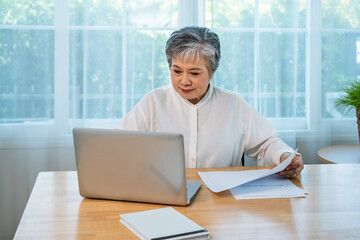 Senior Asian businesswoman manager analyzing documents and working on laptop at office desk