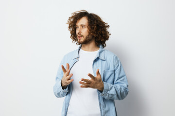 Young man with curly hair expressing emotions while gesturing in a light denim jacket against a...