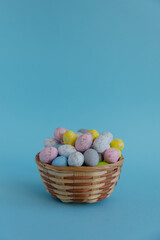 On a blue background, there is a wicker basket filled with Easter colorful eggs, a place for text, advertising or congratulations. Side view. The concept of the Easter holiday.