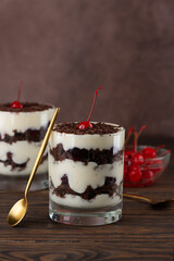 Black forest trifle with cherry, cream with shea butter, cognac and chocolate biscuit in glass on a brown wooden table. Vegan dessert. Vertical orientation.