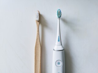 Comparison of a manual toothbrush alongside an electric toothbrush on a light surface