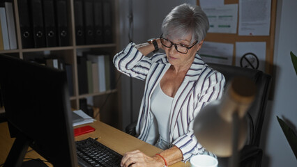 Woman with short grey hair in a striped blazer sitting in an office, holding her neck in discomfort...