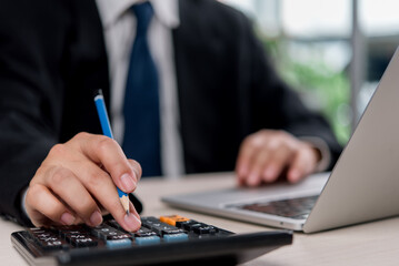 Fototapeta premium businessperson handling financial with a calculator and pencil, surrounded by business documents and a laptop. bookkeeping payroll and budget tax. accounting investment planning and strategy.