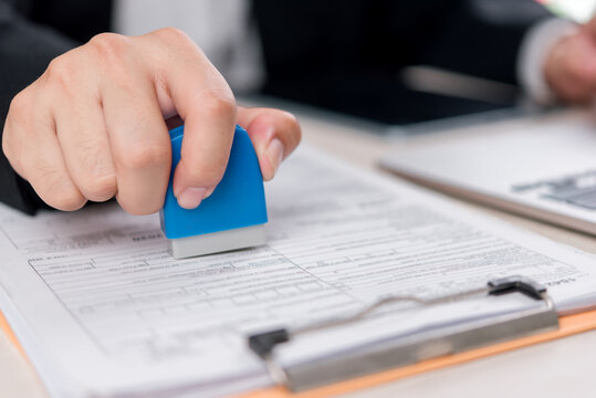 A corporate worker applying a stamp to an official document in the office, showcasing the business process of document approval and paperwork handling.