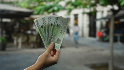 Street view shows man holding south korean won banknotes in hand with cityscape background,...