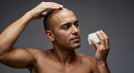 Bald man applying moisturizer cream, African American male skincare routine, self-care and grooming concept against gray background