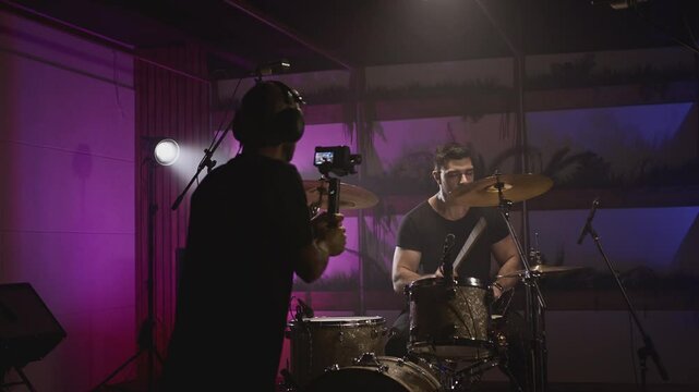 Shooting a music video. The director of photography makes a video, shoots a drummer musician. The view behind the scenes. Create a music video for a rock band. Creative director and crew.
