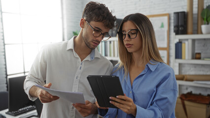Man and woman analyzing documents in a modern office setting with technical equipment and a...