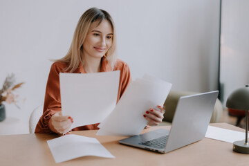 Woman reviewing documents at a desk with a laptop in a calm workspace during daytime