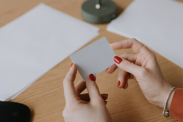 Person holds a blank card while seated at a wooden table surrounded by stationery in a cozy indoor...