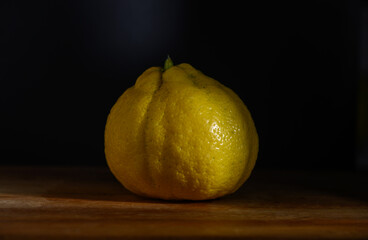 Unique yellow lemon rests on a wooden surface under soft lighting in an artistic still life composition