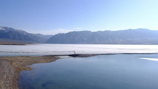 A female tourist walks along a rocky spit between water and ice on the Bartogay Reservoir or lake on the Chilik River in Almaty region in early spring.