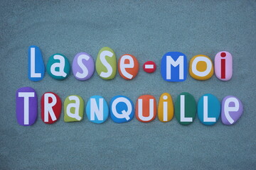 Lasse-moi tranquille, french phrase meaning leave me alone, creative text composed with multi colored hand painted stone letters over green sand