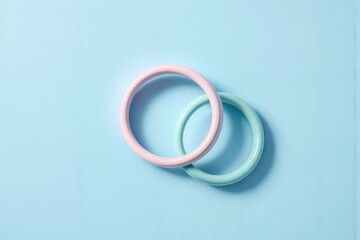 Minimalistische Komposition mit pastellrosa und mintgrünen ineinander verschlungenen Ringen auf pastellblauem Hintergrund als Symbol für Einheit und Verbindung.