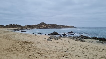 Fototapeta premium Breathtaking view of Chile’s Pacific coast, featuring rugged rocks, golden sandy beach, and waves under a bright sky. Perfect for travel, nature, and coastal landscapes.
