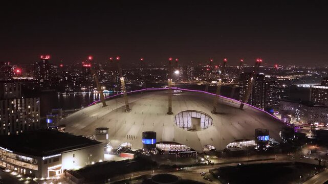 Aerial drone view panning backwards from the O2 Arena in Greenwich in London city at night.