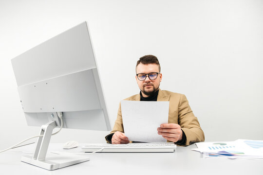 A businessman at a computer in an office, analyzing stock market and inflation charts, sorting through papers. The concept is to capture the tense decision-making process in times of economic instabil